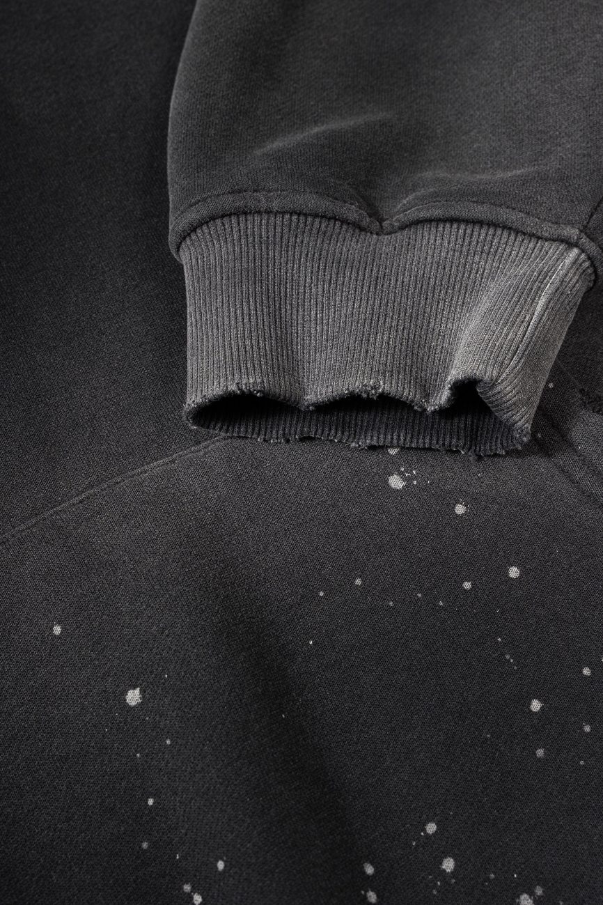 A close-up of the Fusion Core - Vintage Wash Frayed Fleece Hoodie (360 GSM) shows a black sleeve with a frayed cuff and white paint splatters, highlighting the edgy details of this affordable luxury piece.