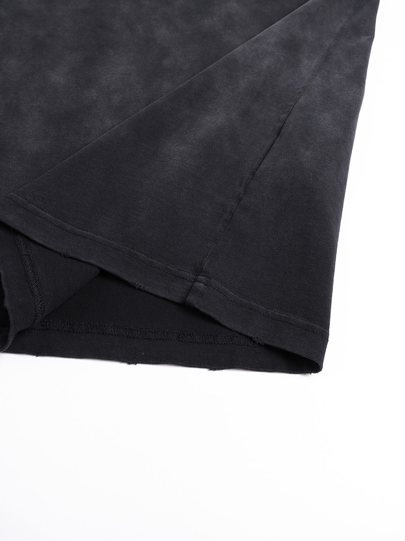 Close-up of the hem and side seam of the Victim - Vintage Washed Hand-Frayed T-Shirt in black, laid flat on a white surface to highlight its unique hand-frayed edges, detailed stitching, and premium fabric texture—ideal for affordable luxury seekers.