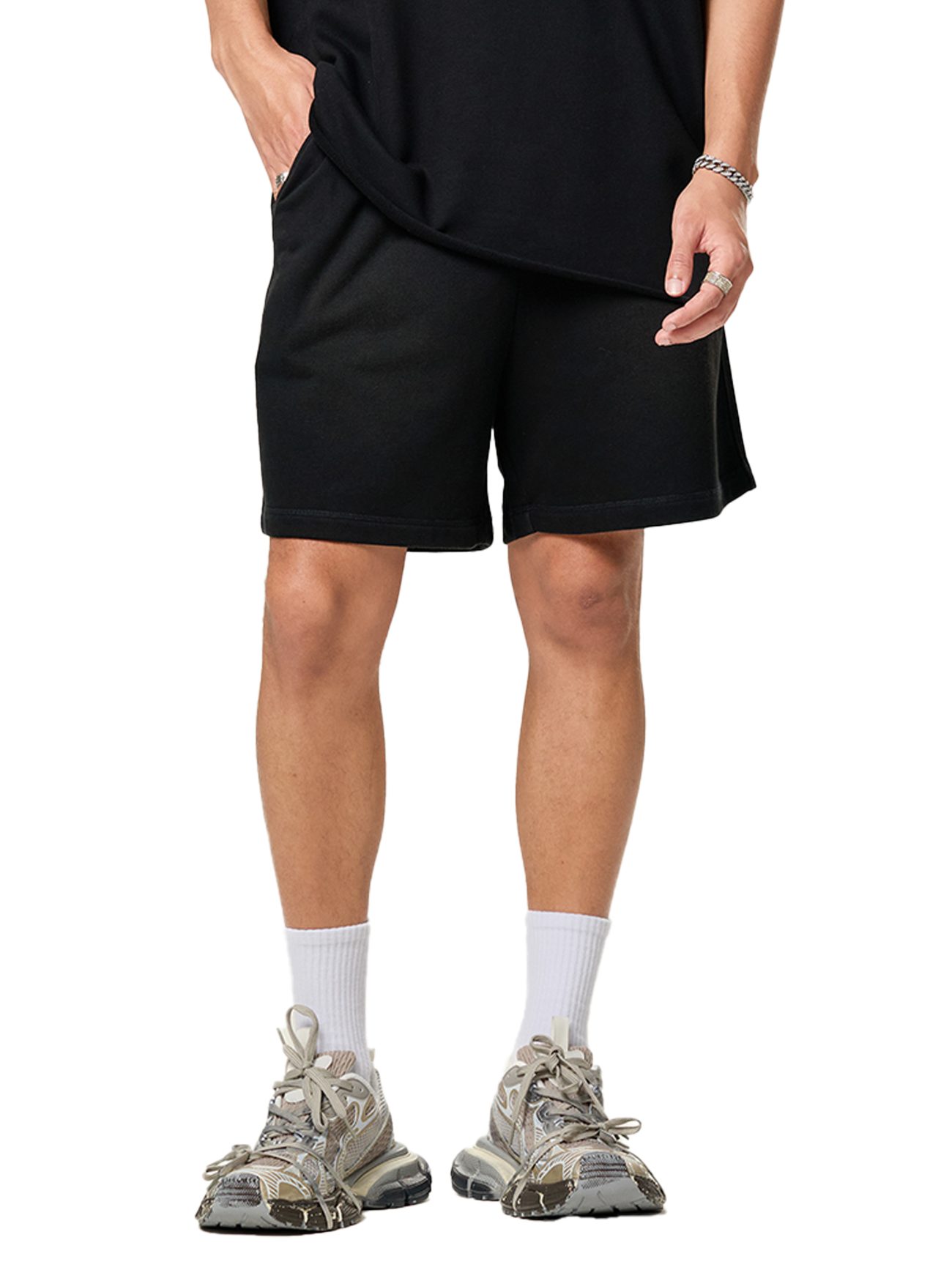Showcasing affordable luxury attire, the lower half of a person is seen in Sun Fade Raw Edge Cotton Shorts paired with a black t-shirt, white crew socks, and gray athletic sneakers against a white background.