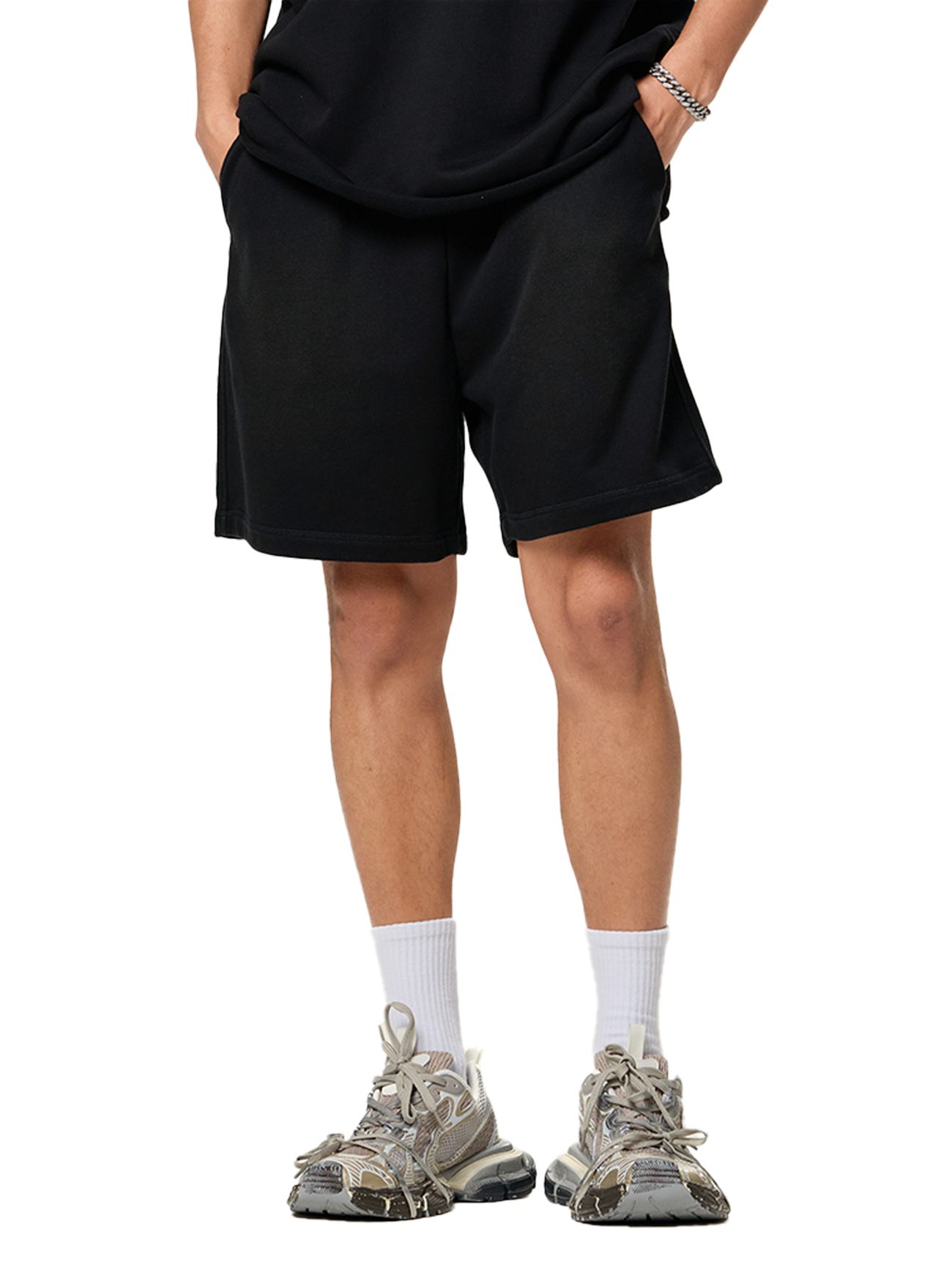 A person wearing affordable luxury stands with hands in pockets, shown from the waist down in Sun Fade Raw Edge Cotton Shorts paired with a black t-shirt, white socks, and gray sneakers.