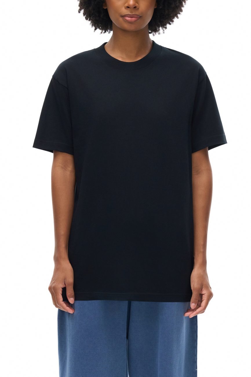A person with short curly hair wears the Fusion Oversized T-shirt and loose blue pants, showcasing affordable luxury clothing against a white background.