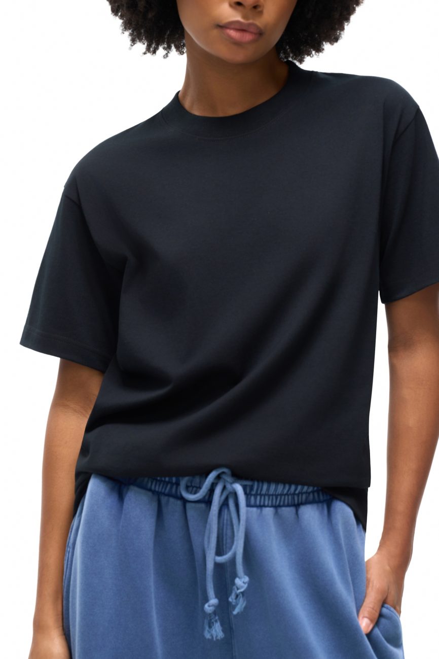 A person wearing the Fusion Emblem - Oversized T-shirt in black and blue drawstring sweatpants stands against a white background. Their face is partially visible, showcasing an affordable luxury clothing ensemble.