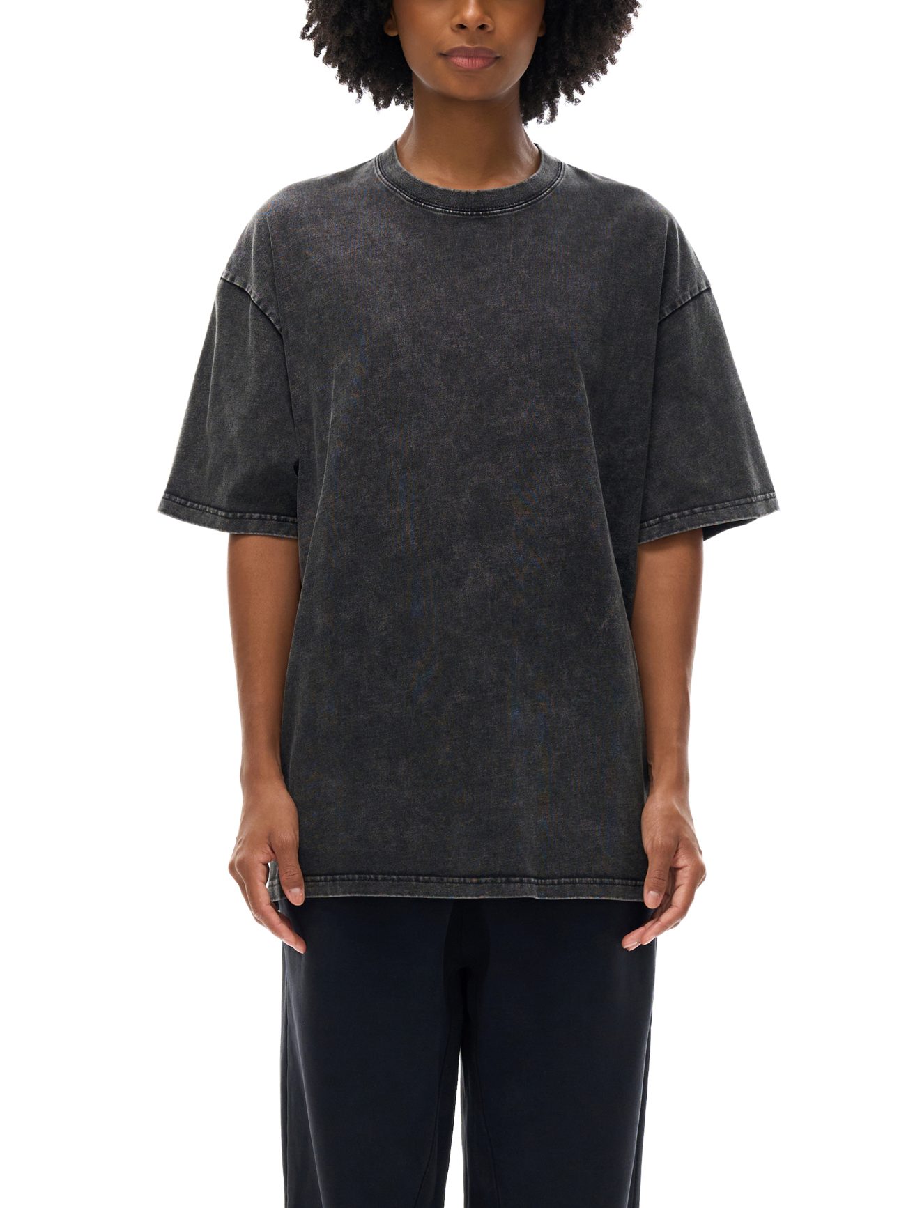 A person with medium brown skin and curly hair wears the Acid Wash Oversize T-Shirt - 250 GSM in washed black, paired with dark pants—showcasing relaxed, affordable luxury—posed against a white background with their face partially out of frame.