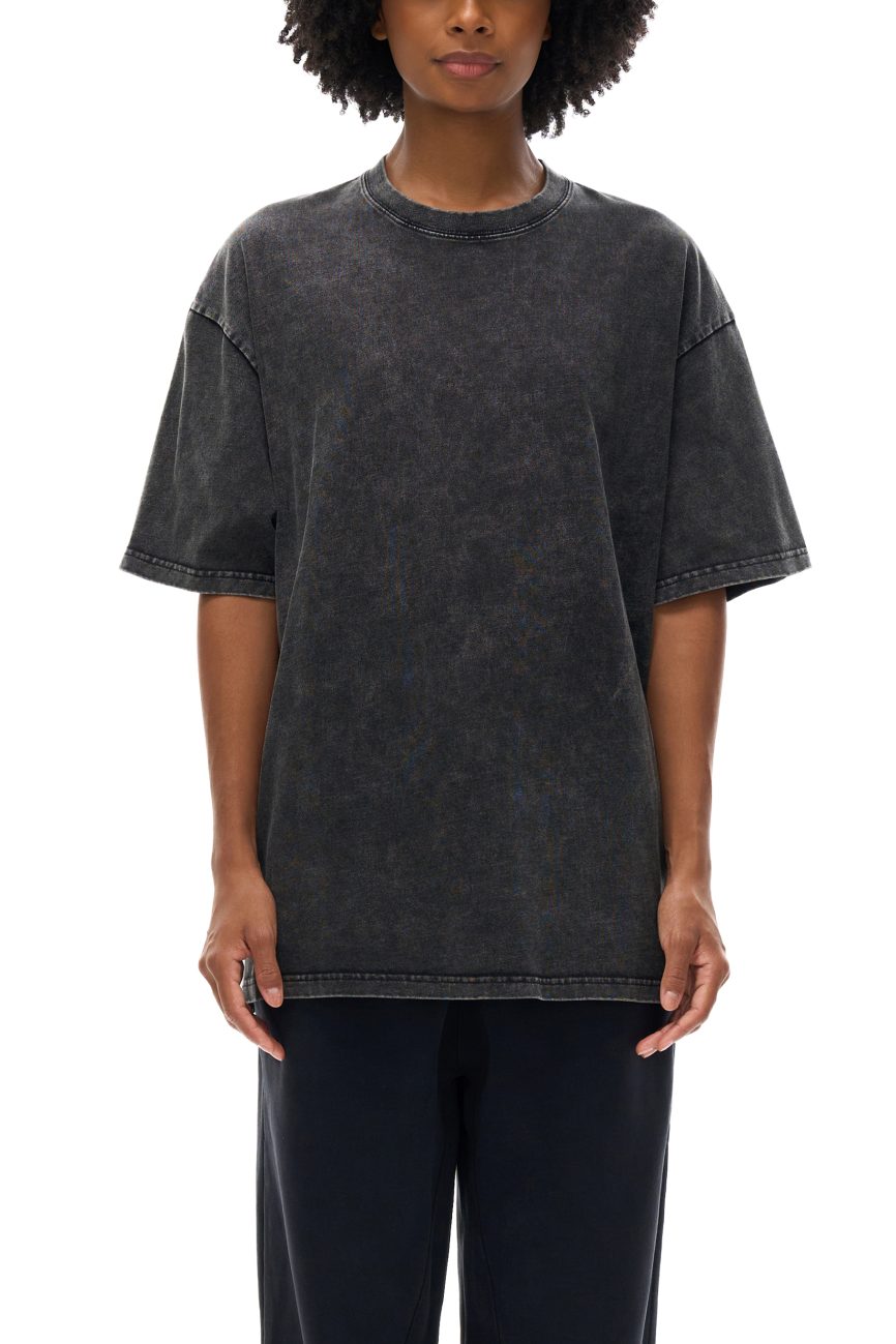 A person with medium brown skin and curly hair wears the Acid Wash Oversize T-Shirt - 250 GSM in washed black, paired with dark pants—showcasing relaxed, affordable luxury—posed against a white background with their face partially out of frame.