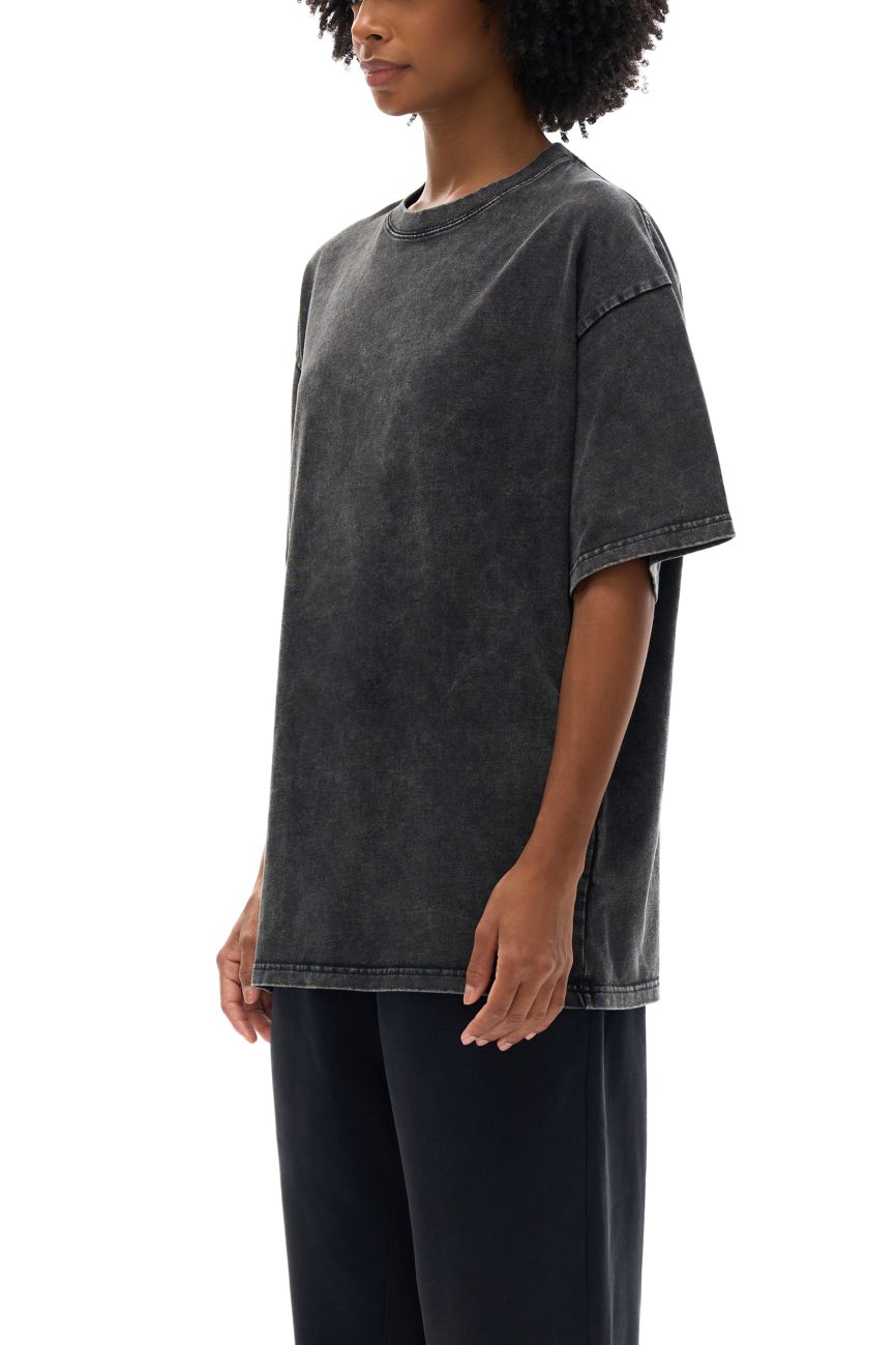 A person stands in profile wearing the Acid Wash Oversize T-Shirt - 250 GSM, styled effortlessly with dark pants. Their curly hair and relaxed pose complete the look against a white background, capturing modern, understated style.