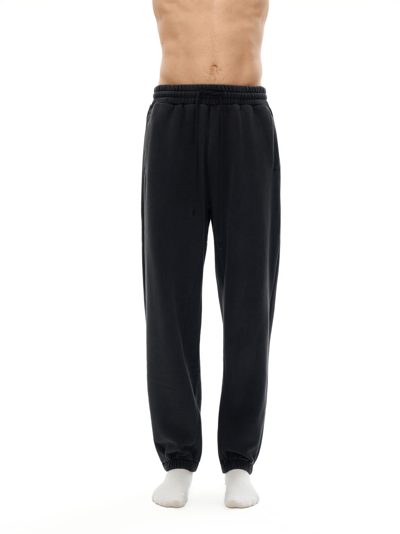 A person wearing Fusion Core - Fleeced Jogger Sweatpants in black and white socks, shown waist to feet against a plain white background. These sweatpants offer affordable luxury for style and comfort lovers. Upper body not visible.