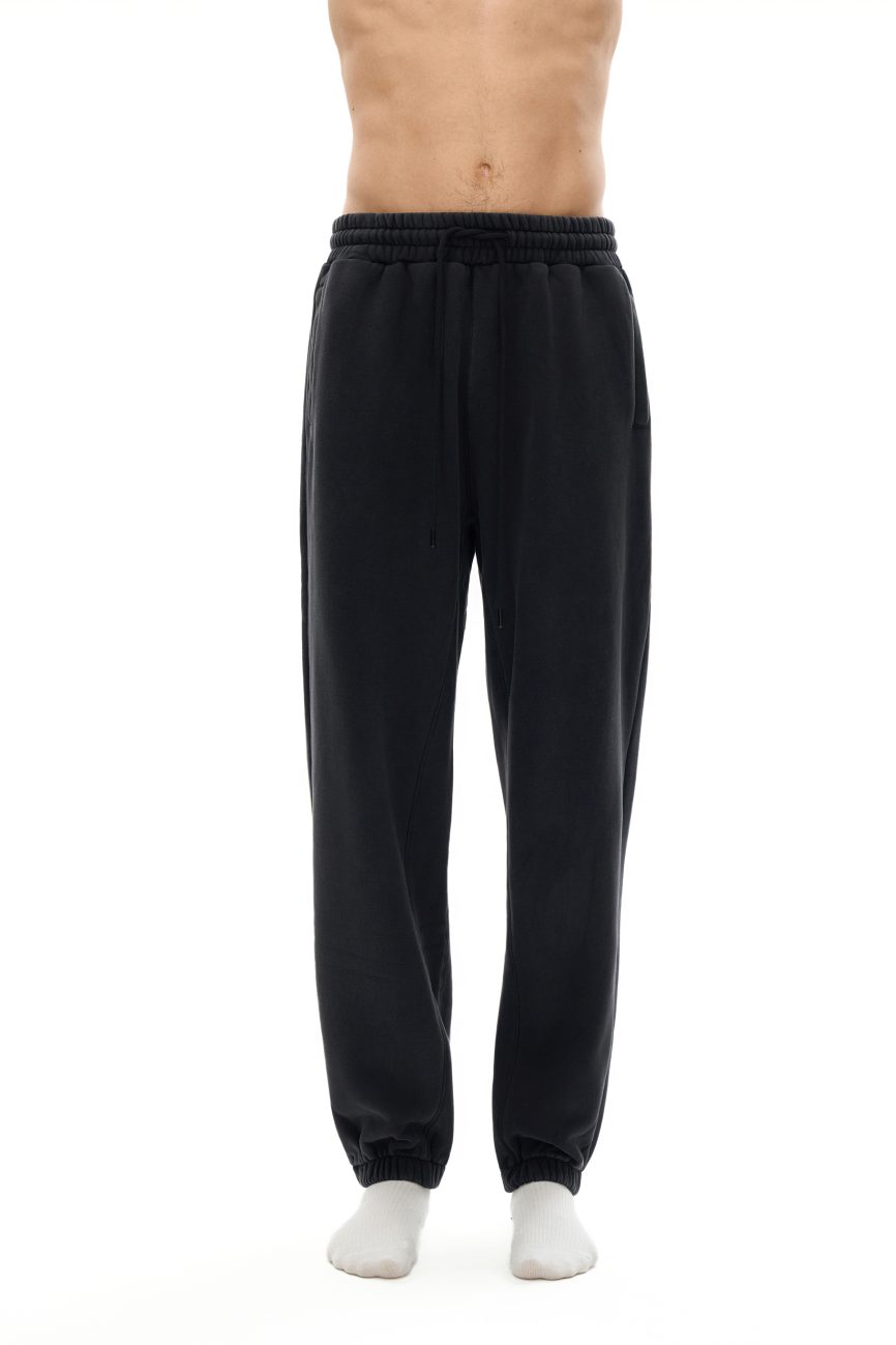 A person wearing Fusion Core - Fleeced Jogger Sweatpants in black and white socks, shown waist to feet against a plain white background. These sweatpants offer affordable luxury for style and comfort lovers. Upper body not visible.