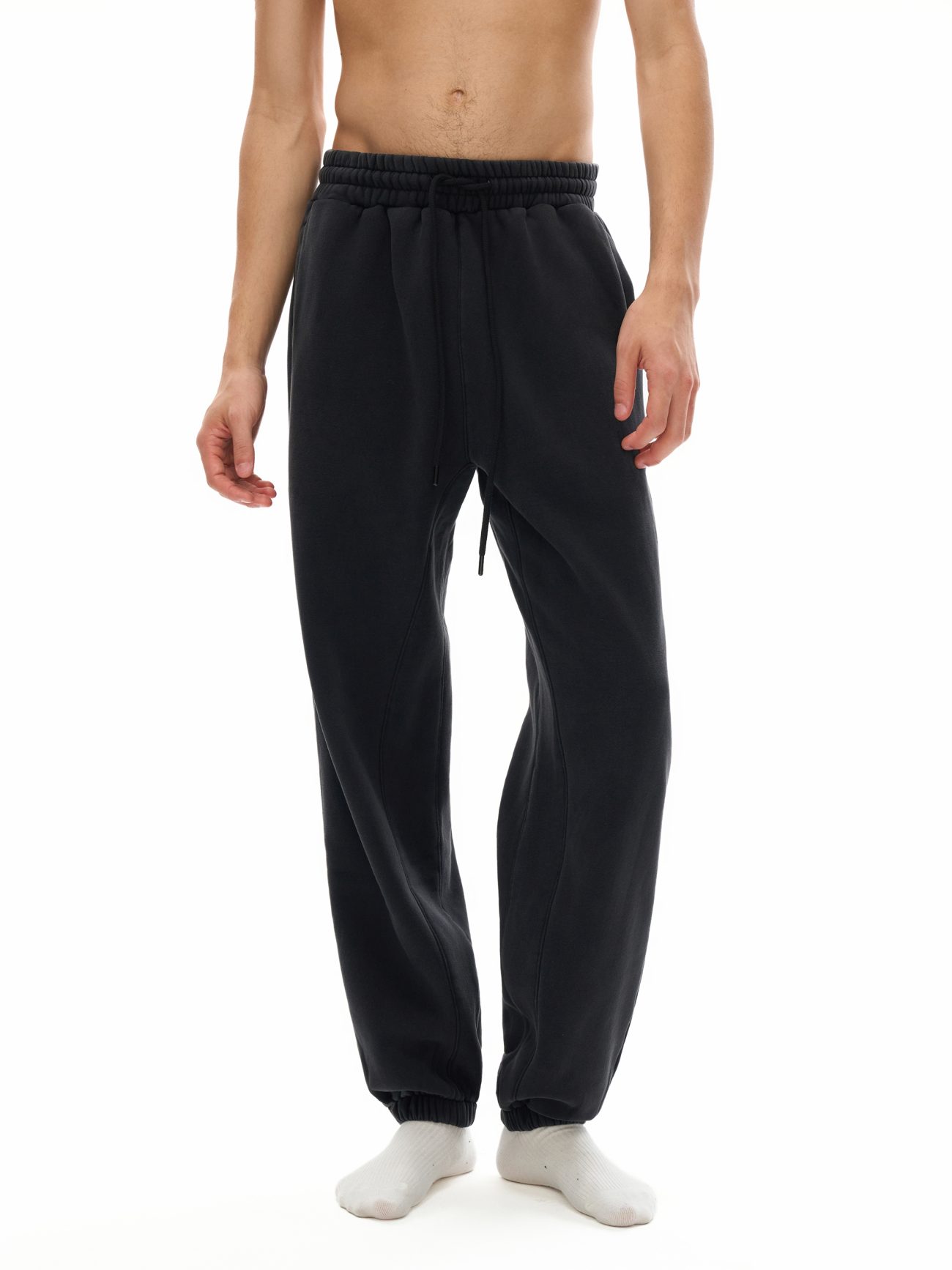A person shown from mid-chest down, wearing Fusion Core - Fleeced Jogger Sweatpants in black with white socks against a white background—showcasing the essence of affordable luxury clothing.