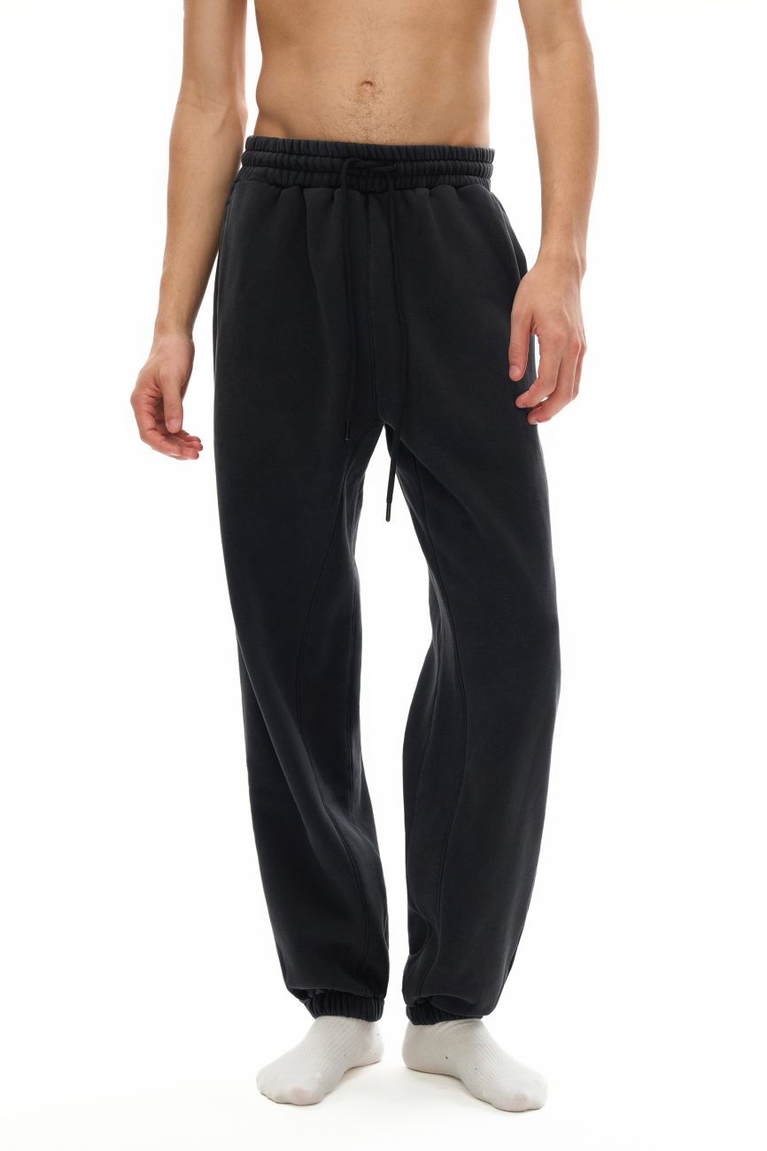 A person shown from mid-chest down, wearing Fusion Core - Fleeced Jogger Sweatpants in black with white socks against a white background—showcasing the essence of affordable luxury clothing.