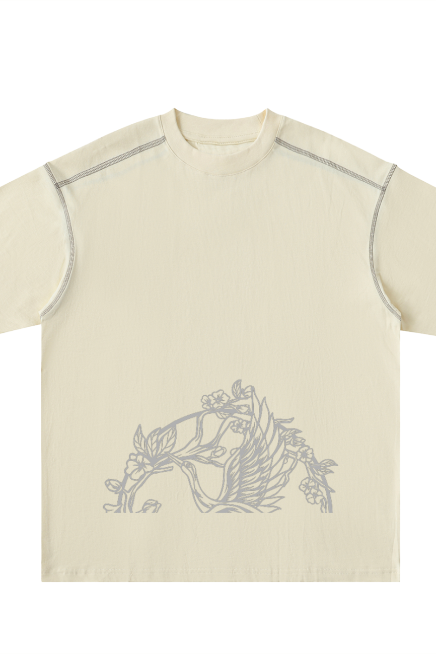 The Crane Oversized Contrast-Stitched Cotton Tee in beige features gray floral and leaf line art near the hem, plus visible seam details on the shoulders and sleeves for an understated, elevated look.