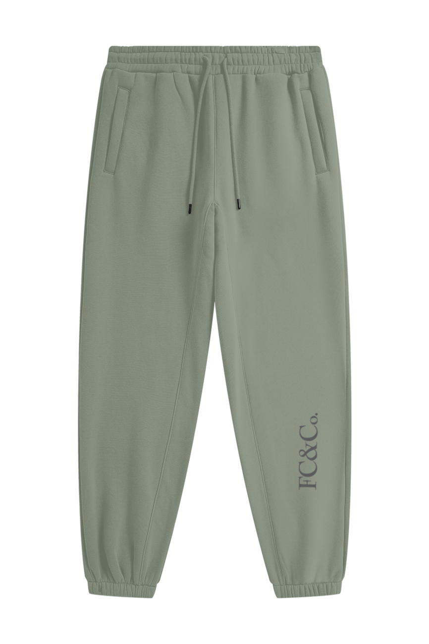 Streetwear Unisex Fleece Joggers in sage green feature an elastic waistband, drawstring, side pockets, cuffed ankles, and subtle FC & Co. text near the left ankle—affordable luxury for everyday comfort.