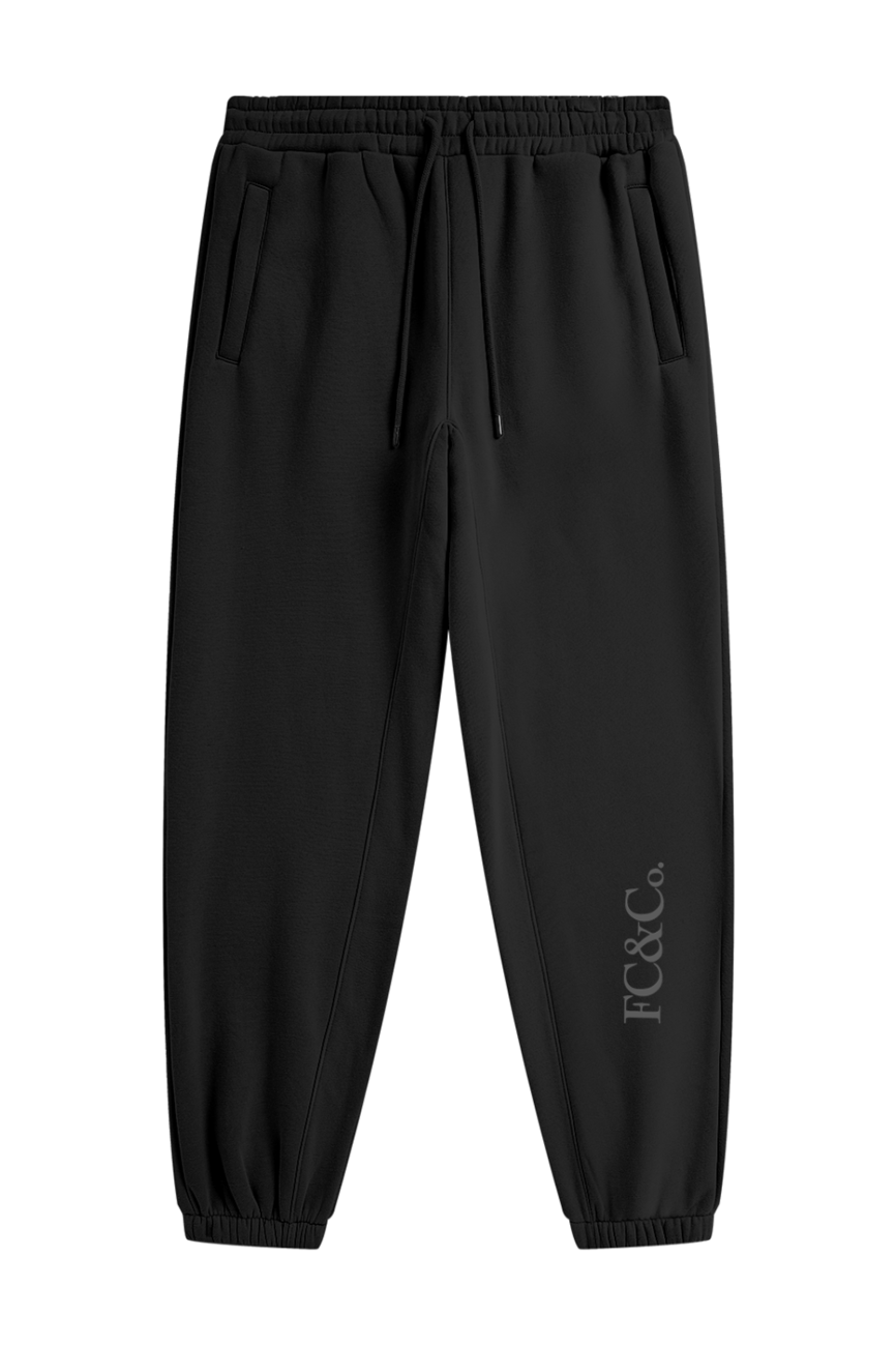 Streetwear Unisex Fleece Joggers feature an elastic waistband, drawstring, two side pockets, cuffed ankles, and subtle FC&Co. print near the left ankle—offering comfort and affordable luxury in black.