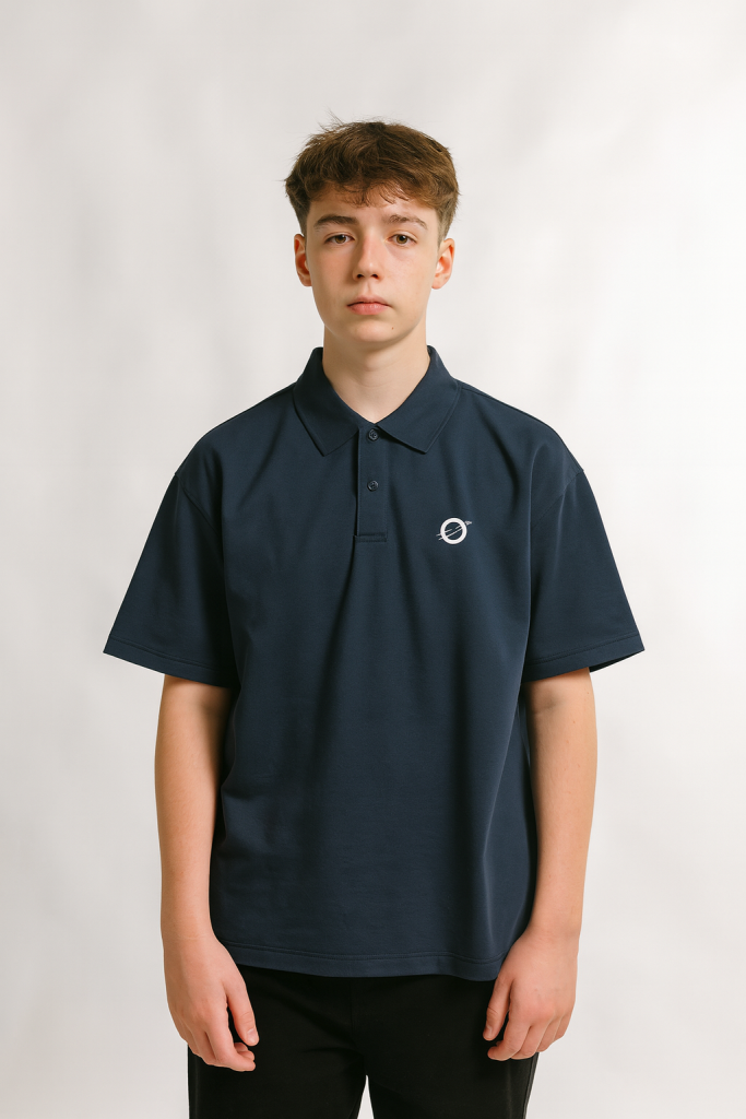 A teenage boy with light brown hair stands against a white background, wearing the Fusion Drop Shoulder Short-Sleeve Polo in navy blue with a small white circular logo and black pants, looking straight at the camera with a neutral expression.