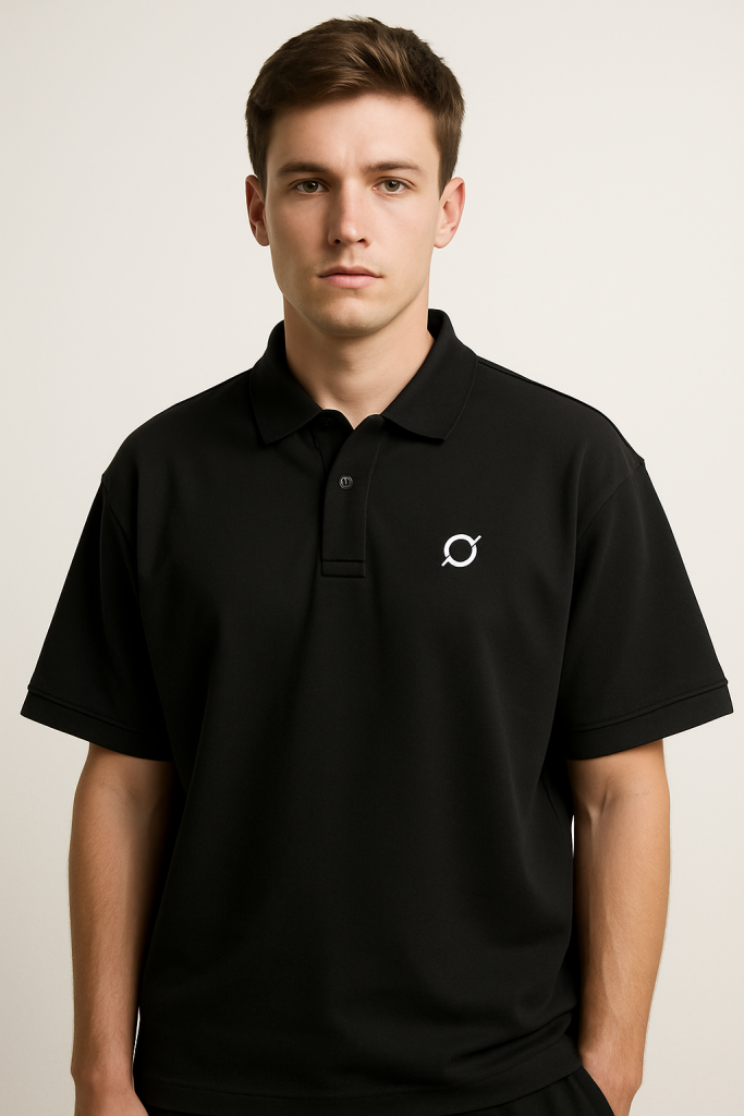 A young man with short brown hair wears the Drop Shoulder Short-Sleeve Polo in black, featuring a small white logo on the left chest. He stands against a plain light background, looking directly at the camera with a neutral expression.