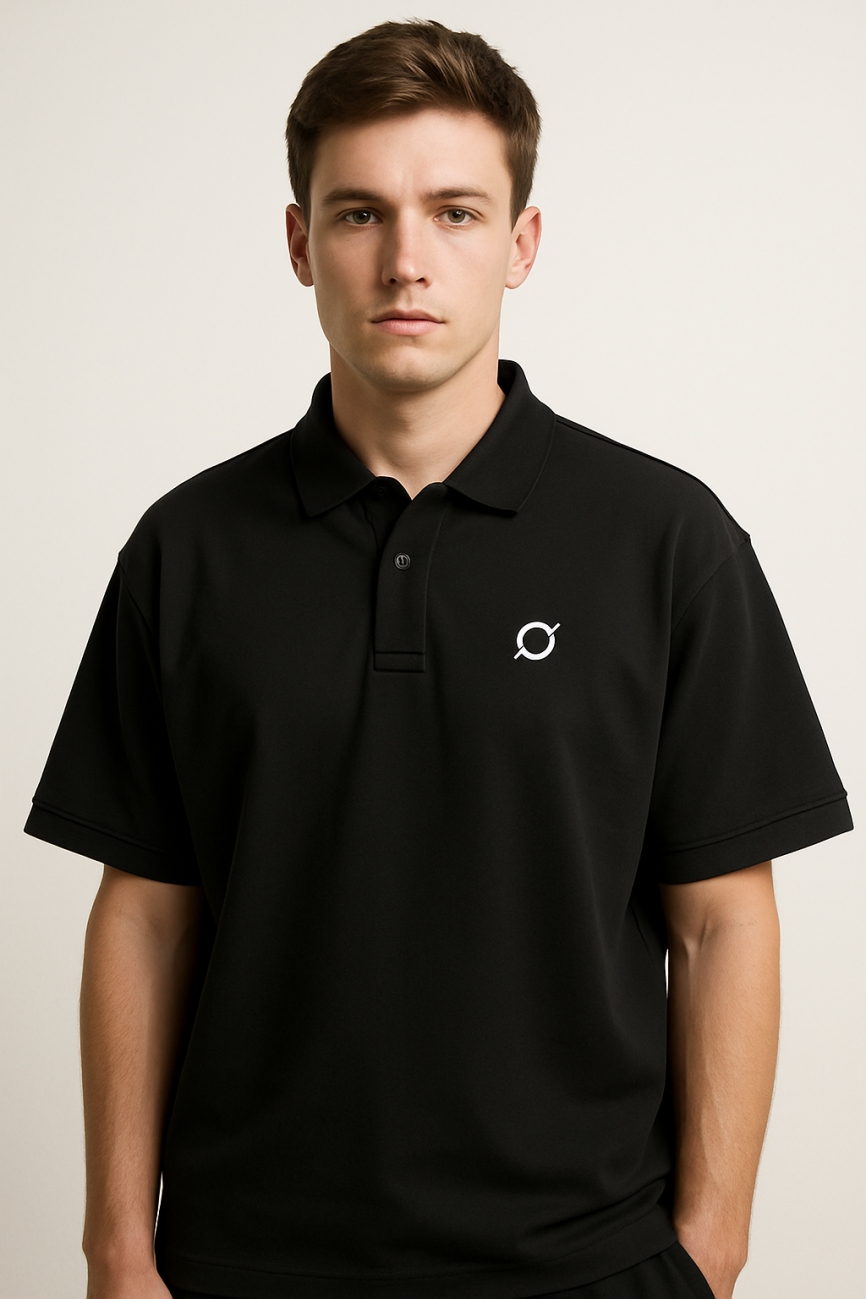A young man with short brown hair wears the Drop Shoulder Short-Sleeve Polo in black, featuring a small white logo on the left chest. He stands against a plain light background, looking directly at the camera with a neutral expression.