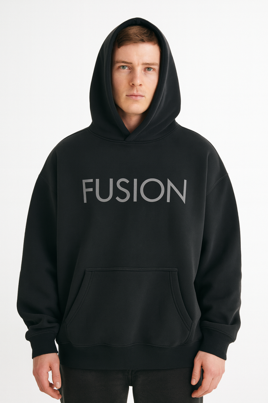 A person wearing the Fusion Oversize Fleeced Hoodie with the hood up stands against a plain white background. The affordable luxury hoodie is black and features FUSION in large gray letters across the chest.