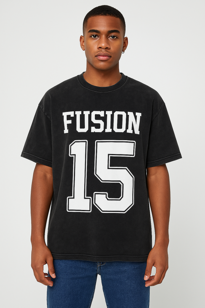 A young man with short hair faces forward, wearing the Acid Wash Oversize T-Shirt - 250 GSM in black from the Affordable Luxury Clothing line. It features bold white FUSION and the number 15 on the front, paired with blue jeans.
