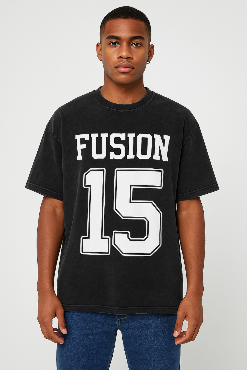 A young man with short hair faces forward, wearing the Acid Wash Oversize T-Shirt - 250 GSM in black from the Affordable Luxury Clothing line. It features bold white FUSION and the number 15 on the front, paired with blue jeans.