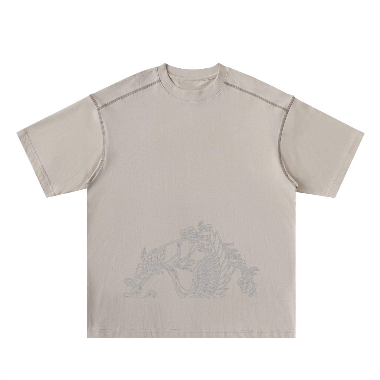 The Crane - Oversized Contrast-Stitched Cotton Tee features a beige, short-sleeve design with subtle light gray floral line art near the bottom front and visible shoulder seam stitching for an affordable touch of luxury.