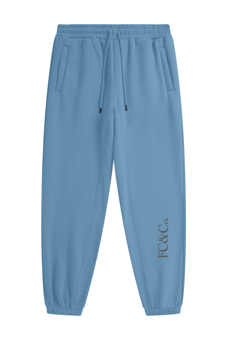 The Streetwear Unisex Fleece Joggers feature light blue fabric, an elastic waistband with drawstring, side pockets, cuffed ankles, and JTC & Co. printed vertically near the lower left leg—blending style and comfort for affordable luxury.