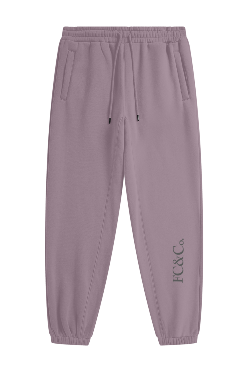 The Streetwear Unisex Fleece Joggers feature a light purple shade, elastic waistband with drawstring, ankle cuffs, two side pockets, and FC&Co. text printed vertically by the left ankle for affordable luxury style every day.
