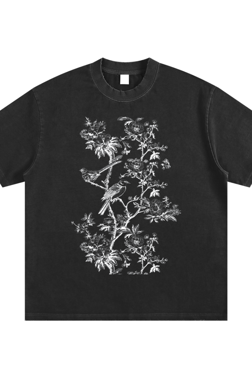 The Toile De Jouy Heavyweight Vintage Washed Frayed T-Shirt features a detailed white botanical and bird illustration on black—an affordable luxury piece that adds exquisite style to your everyday wardrobe.