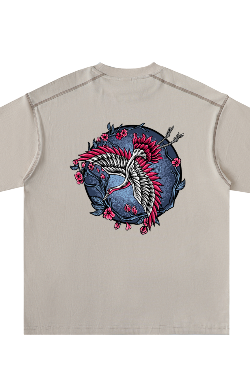 Experience affordable luxury with the Crane - Oversized Contrast-Stitched Cotton Tee, a beige shirt showcasing a white crane, red accents, pink flowers, and dark branches on a circular blue background.