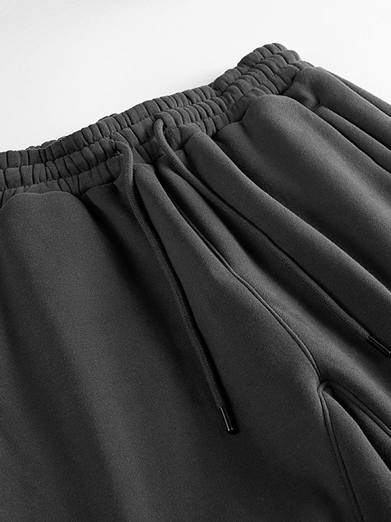 Close-up of the Streetwear Unisex Fleece Joggers in black, featuring an elastic waistband with gathered fabric and a drawstring with metal tips, laid flat on a white surface—perfect for those seeking affordable luxury.