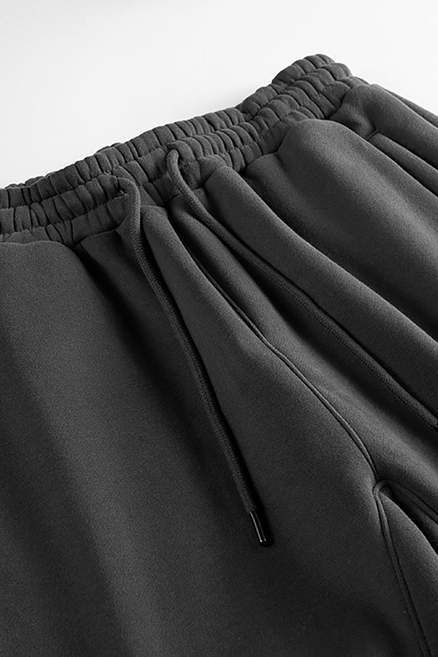 Close-up of the Streetwear Unisex Fleece Joggers in black, featuring an elastic waistband with gathered fabric and a drawstring with metal tips, laid flat on a white surface—perfect for those seeking affordable luxury.