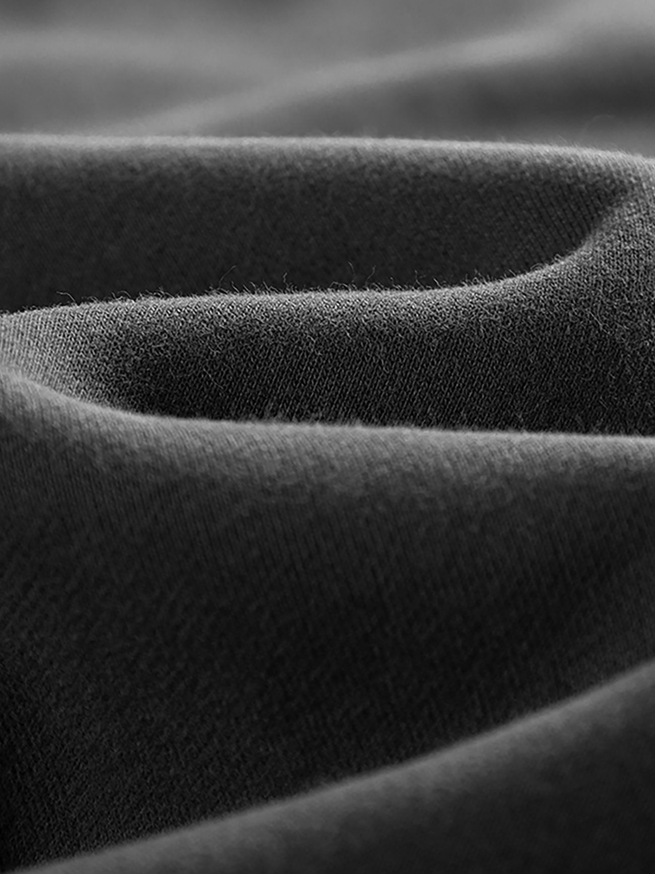Close-up of the soft, black fabric on Streetwear Unisex Fleece Joggers shows gentle folds and a slightly textured surface, highlighting the smooth material and subtle shadows—reflecting affordable luxury quality.