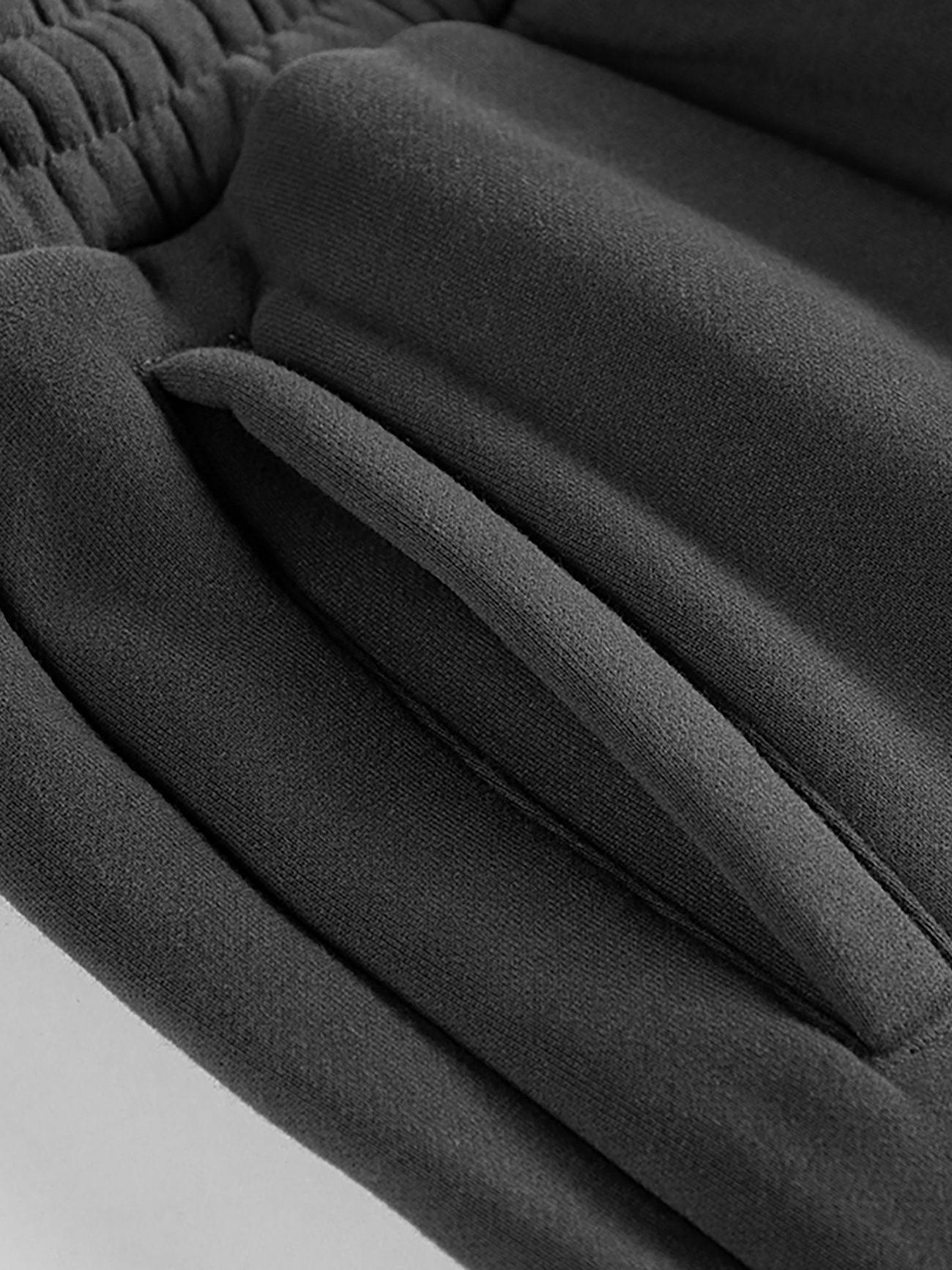 Close-up of black Streetwear Unisex Fleece Joggers, featuring an elastic waistband and slanted side pocket, made from soft, slightly textured fabric—part of our Affordable Luxury Clothing line.