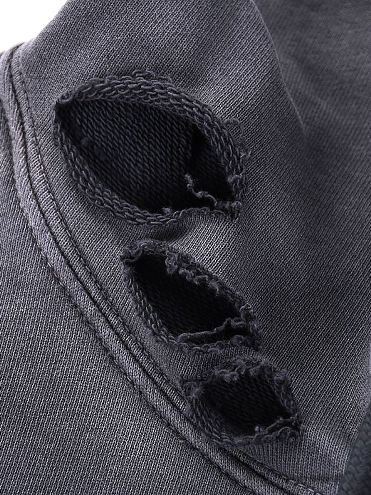 Close-up of the Heavyweight Pure Cotton Hand-Frayed Monkey Washed Hoodie by Company. Black fabric with three rough, oval holes and frayed edges along a seam; texture and stitching are clearly visible.