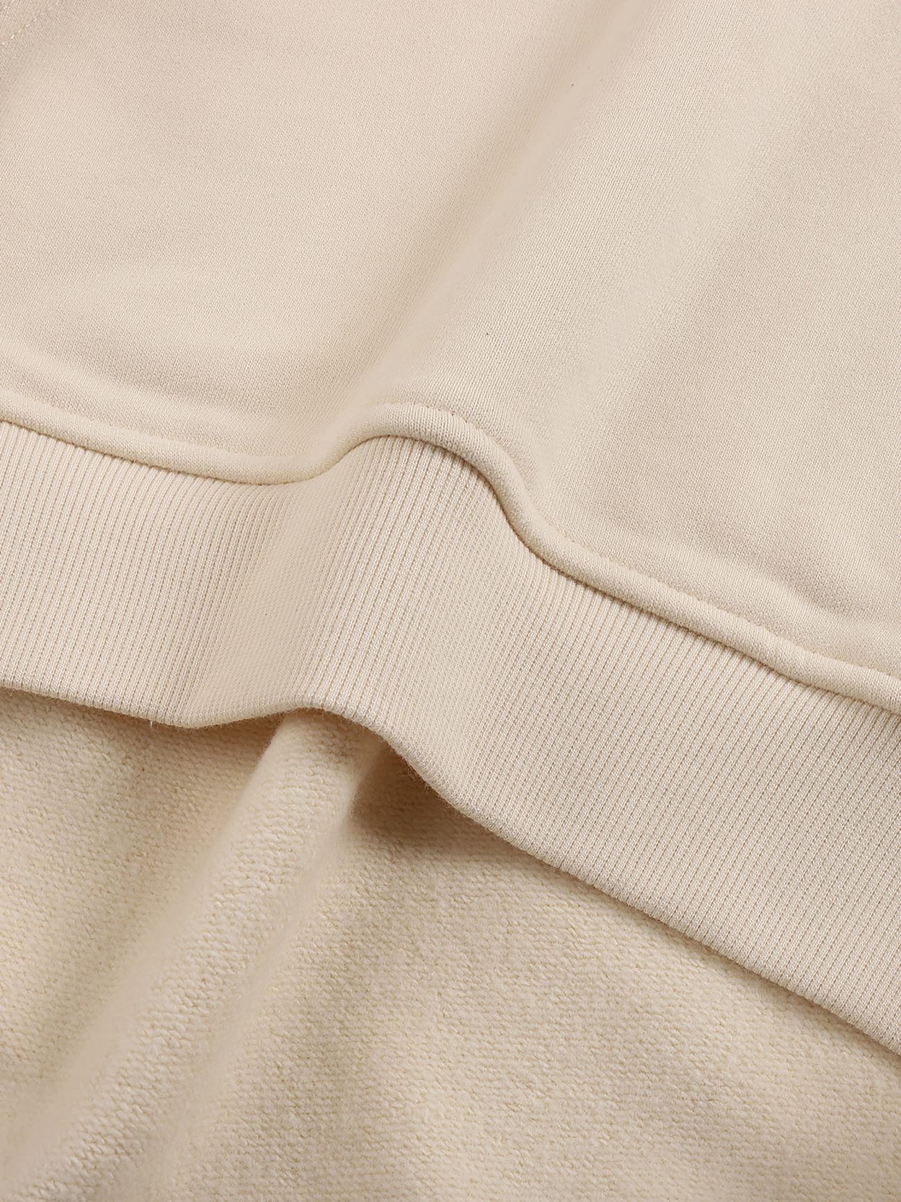 Close-up of the ribbed hem and soft fabric texture of the Fleeced High Neck Hoodie in beige, showcasing detailed stitching—an affordable luxury piece designed for everyday comfort.