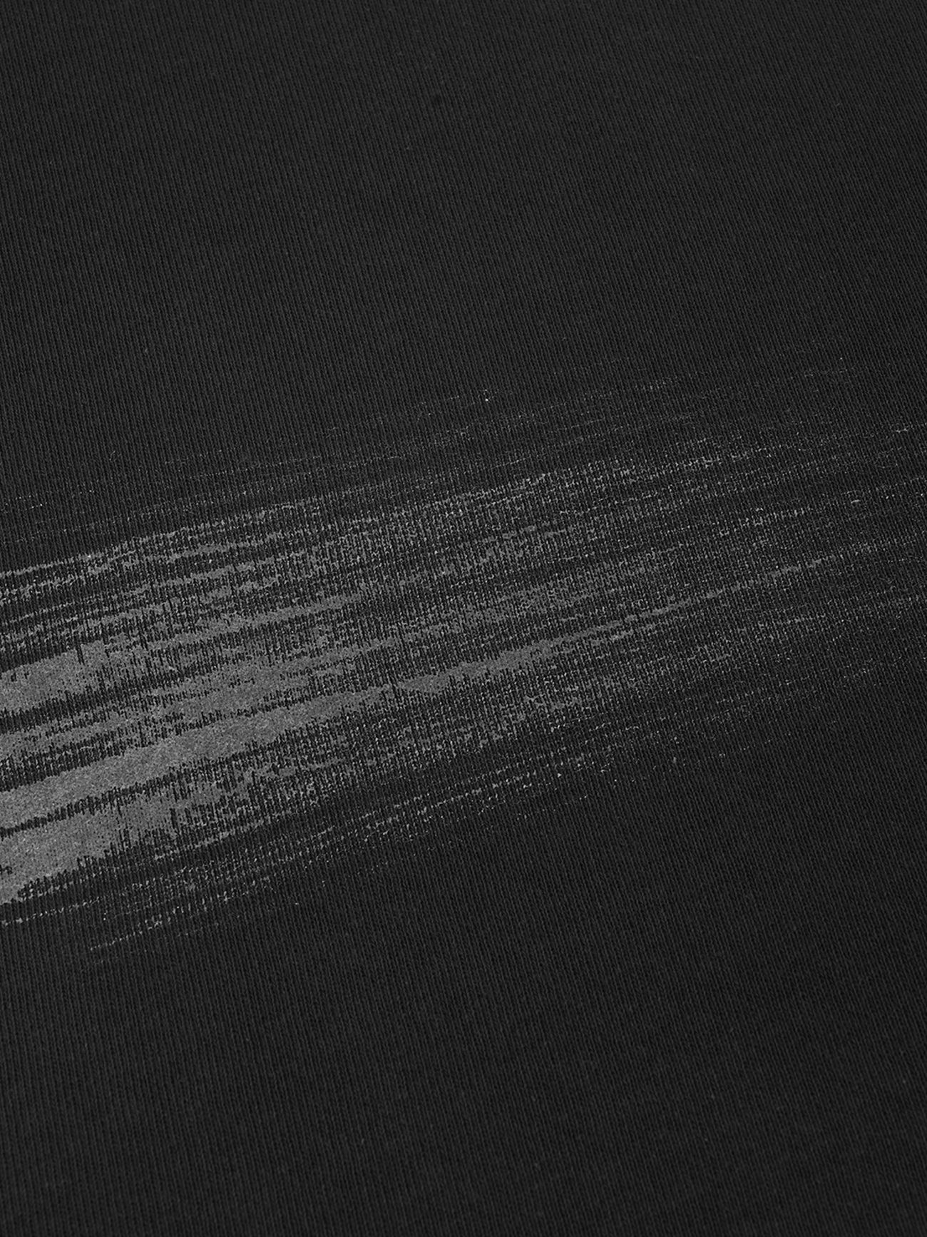 A close-up of our Hand Brushed T-shirt’s black fabric, highlighted by a grayish, horizontal streak across the surface that suggests subtle wear, a smear, or a unique print detail.