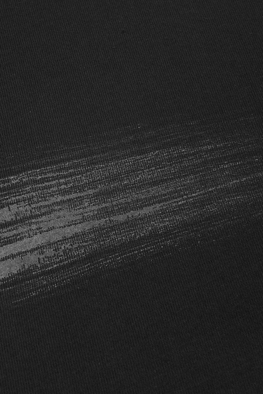 A close-up of our Hand Brushed T-shirt’s black fabric, highlighted by a grayish, horizontal streak across the surface that suggests subtle wear, a smear, or a unique print detail.
