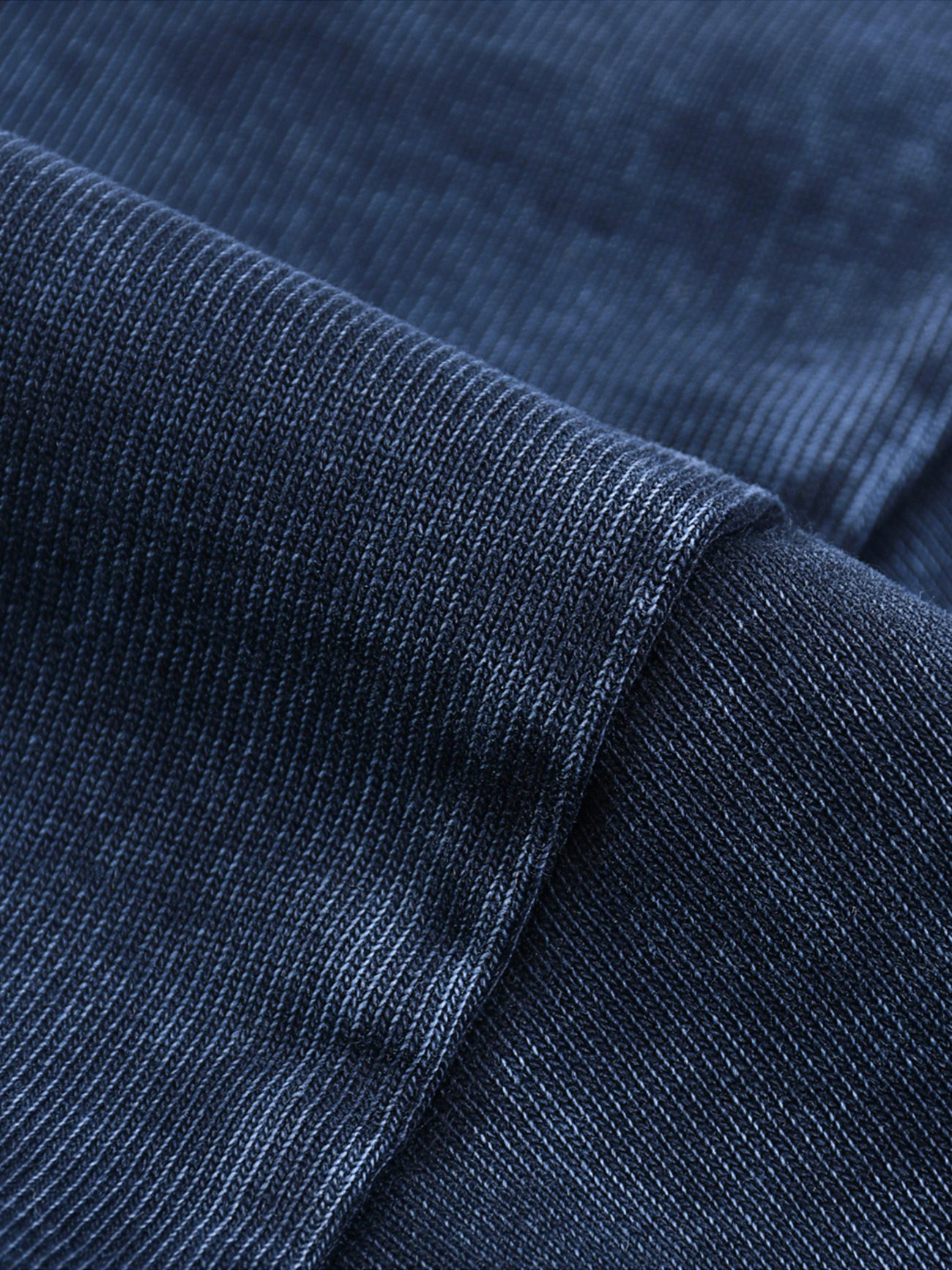 Close-up of the dark blue ribbed fabric on our Fusion Heavyweight Snow-Washed Polo T-Shirt, highlighting its soft, slightly shiny texture and fine horizontal lines, with visible seams and folds for a touch of affordable luxury.