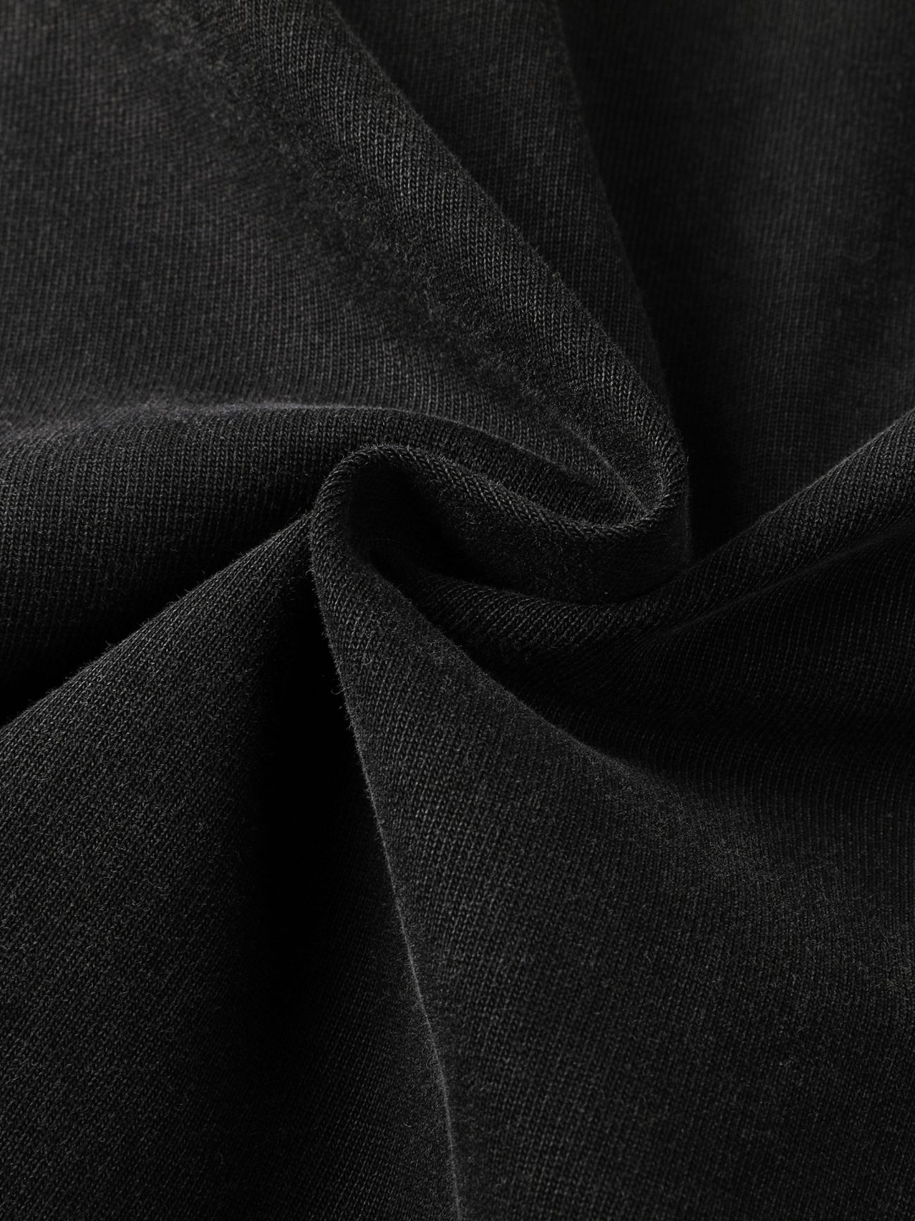 Close-up of black fabric from the Toile De Jouy - Heavyweight Vintage Washed Frayed T-Shirt, featuring soft texture with gentle folds and a central twist that forms a spiral pattern, highlighting smooth, matte elegance in affordable luxury.