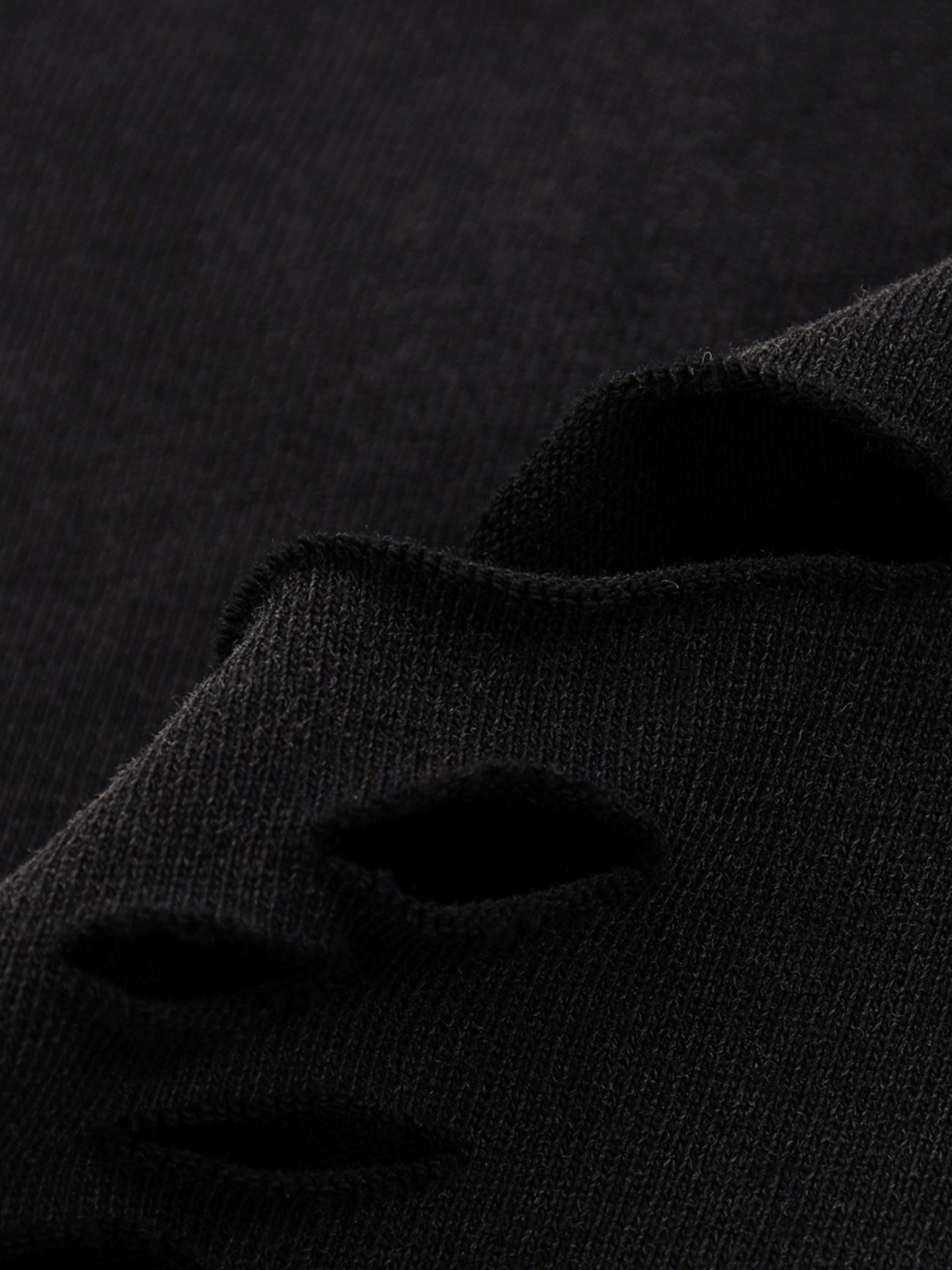 Close-up of black fabric from our Fusion Snow Washed Raw-Hem T-Shirt, showing several horizontal, frayed holes that reveal the torn edges and unique texture of the material.