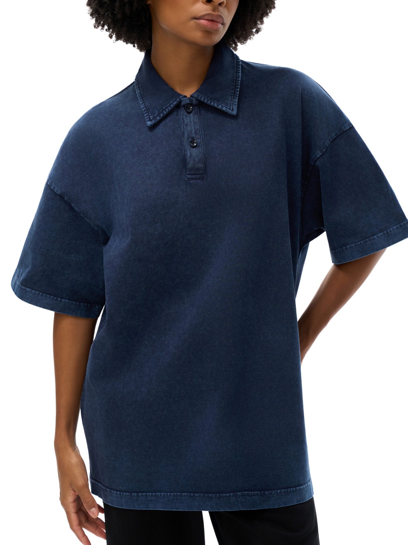 A person wearing the Fusion Heavyweight Snow-Washed Polo T-Shirt—a loose-fitting, short-sleeved, dark blue denim polo that represents affordable luxury—stands confidently with one hand on their hip.