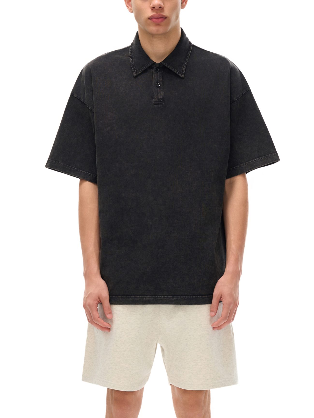 A person wears the Fusion Heavyweight Snow-Washed Polo T-Shirt in black from our Affordable Luxury Clothing line, paired with light beige shorts, standing against a white background with hands resting by their sides.