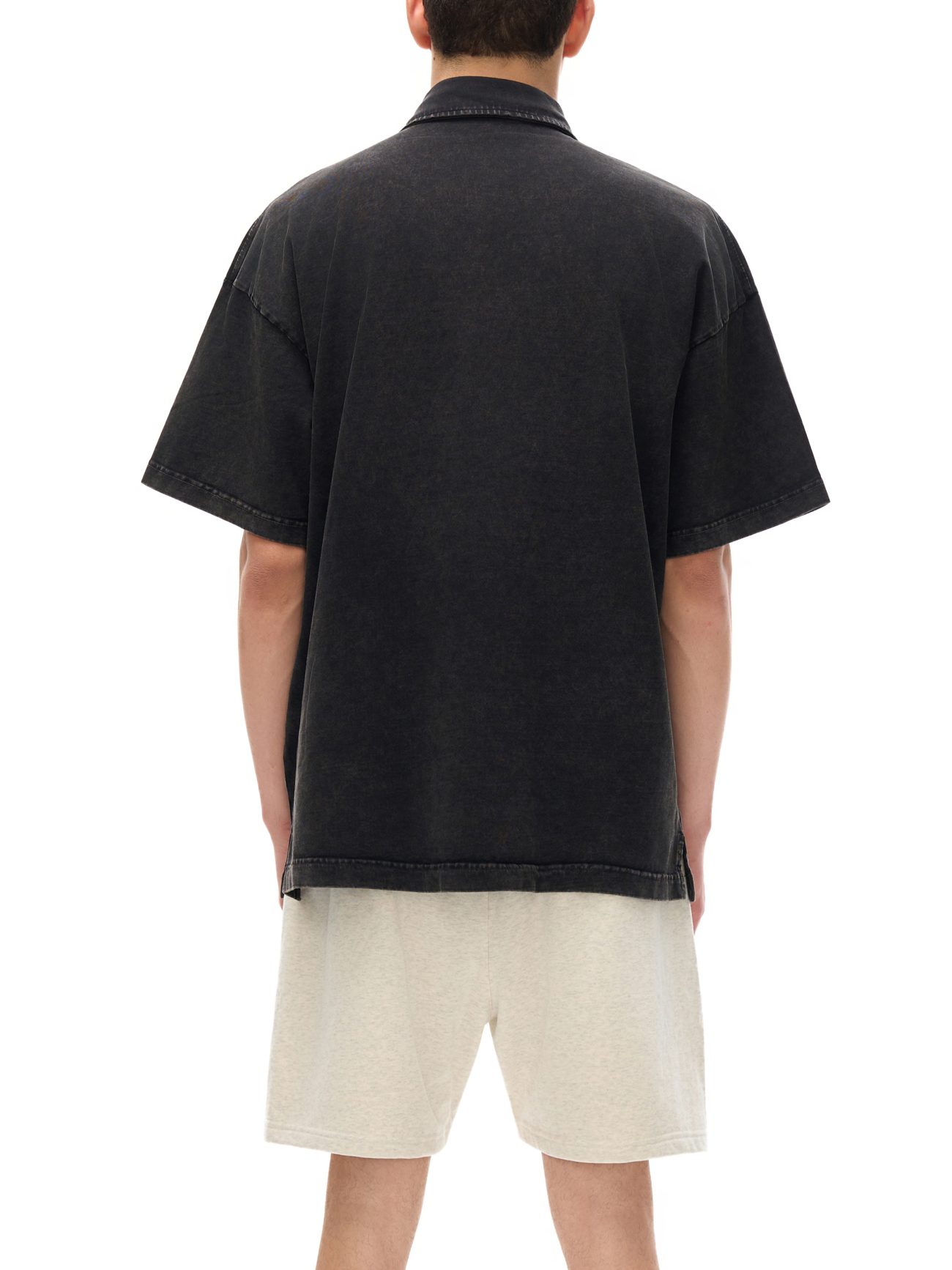 A person faces away from the camera, modeling the affordable luxury Fusion Heavyweight Snow-Washed Polo T-Shirt in black with light beige shorts against a plain white background.