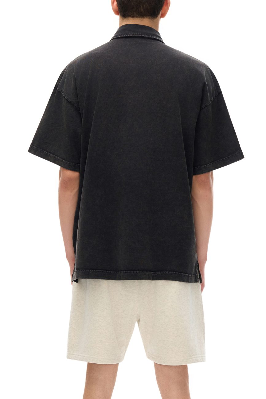 A person faces away from the camera, modeling the affordable luxury Fusion Heavyweight Snow-Washed Polo T-Shirt in black with light beige shorts against a plain white background.