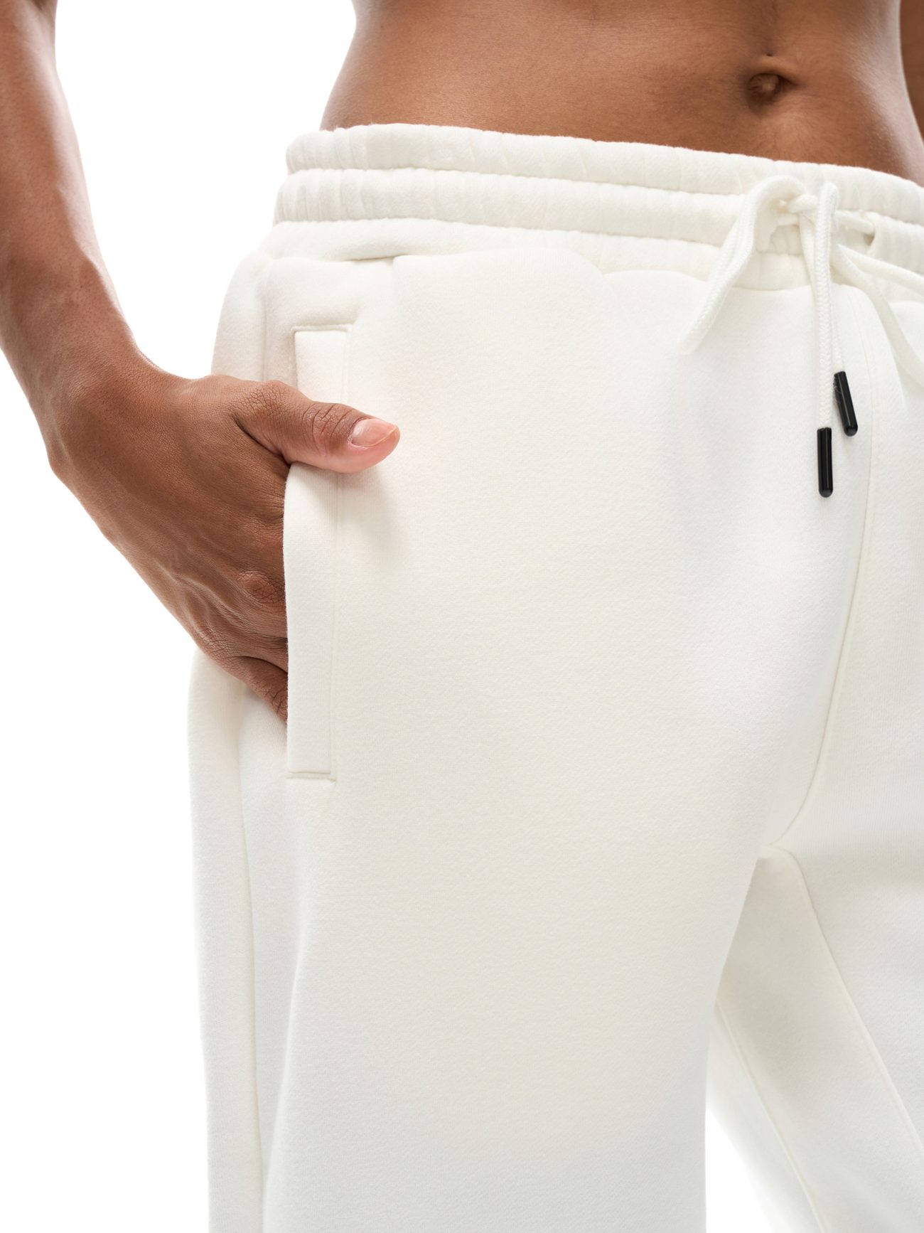 Close-up of a hand in the pocket of Streetwear Unisex Fleece Joggers, highlighting affordable luxury with the soft fabric, drawstring waistband, and a glimpse of bare midriff.