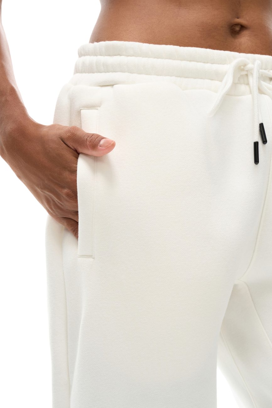 Close-up of a hand in the pocket of Streetwear Unisex Fleece Joggers, highlighting affordable luxury with the soft fabric, drawstring waistband, and a glimpse of bare midriff.