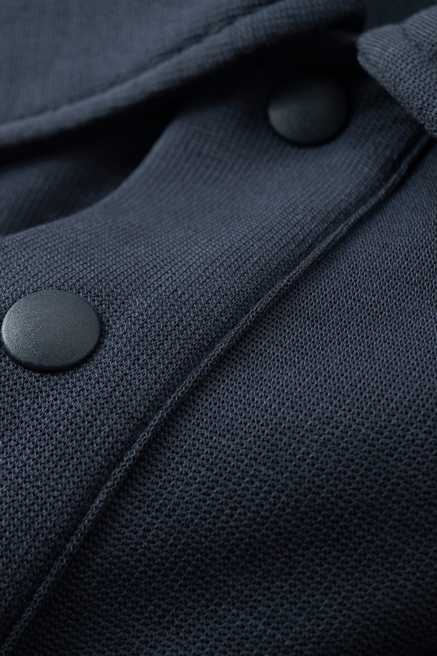 Close-up of the Fusion Drop Shoulder Short-Sleeve Polo’s dark, textured fabric with matte black snap buttons and detailed stitching, highlighting thoughtful design in affordable luxury clothing.