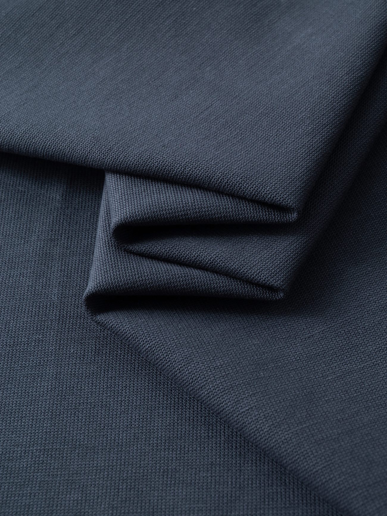 Close-up of dark blue folded fabric with a smooth texture and fine weave, arranged in neat layers—ideal for creating the Fusion Drop Shoulder Short-Sleeve Polo, a perfect choice for affordable luxury clothing.