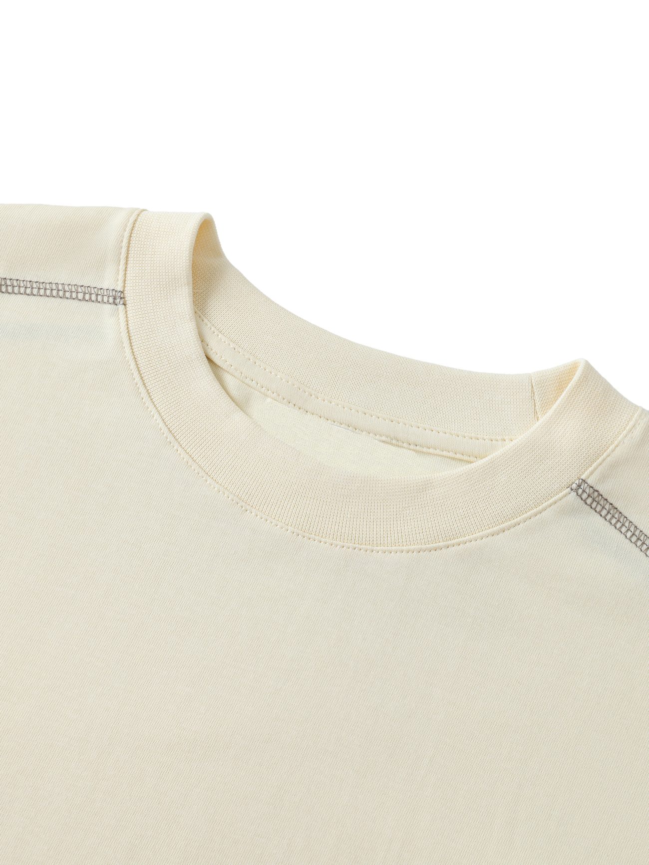 Close-up of the upper portion of our Crane - Oversized Contrast-Stitched Cotton Tee, featuring visible stitching along the shoulder and collar. The soft cream-colored cotton shirt is shown laid flat on a white background.