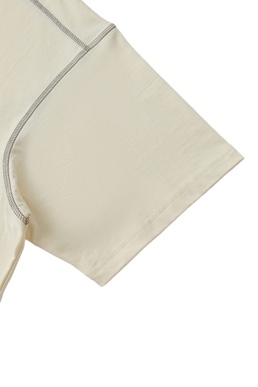 Close-up of the short sleeve and shoulder seam on the Crane - Oversized Contrast-Stitched Cotton Tee, showcasing visible stitching and smooth light beige cotton fabric.