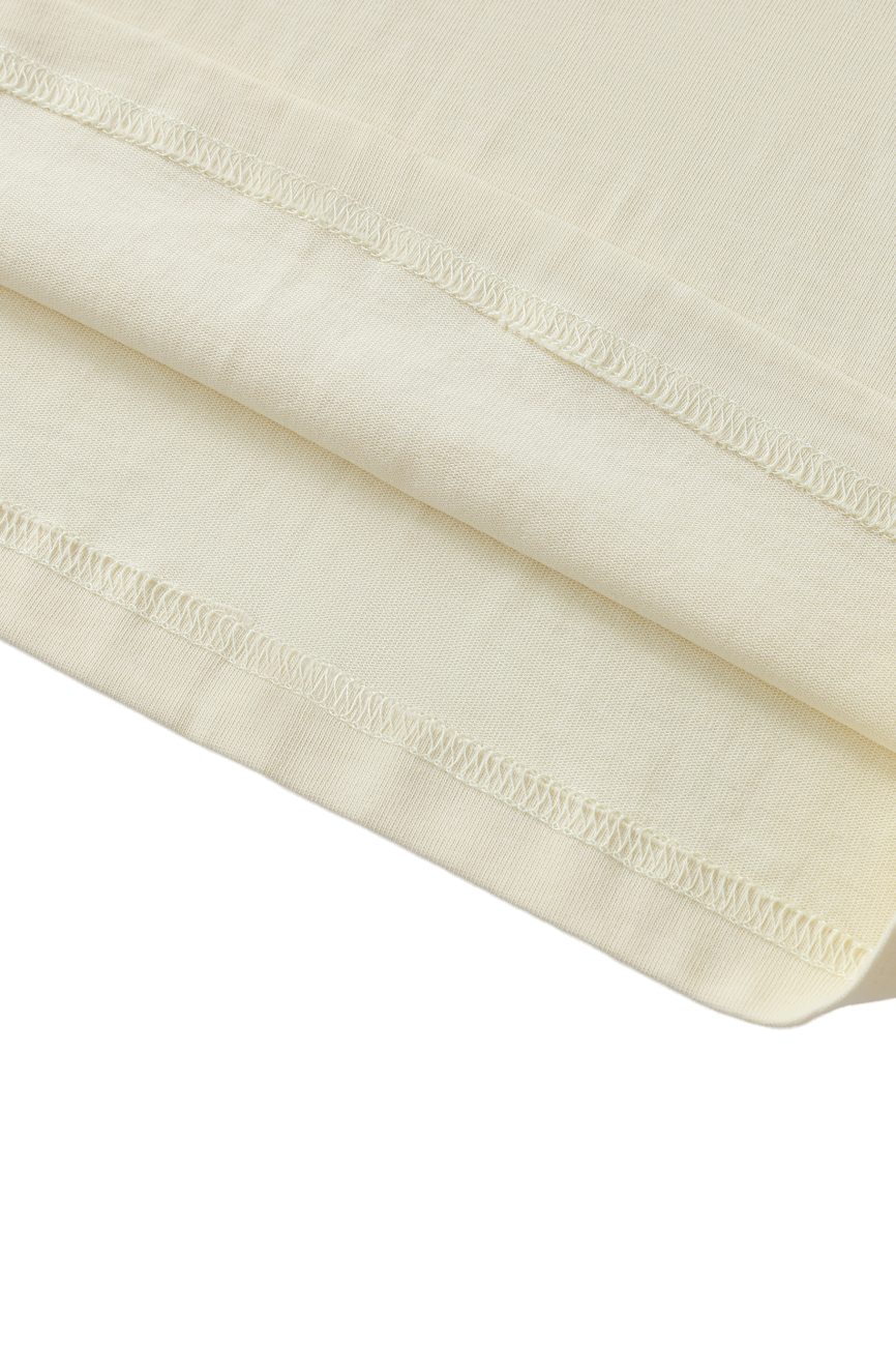 Close-up of the hem on the Crane Oversized Contrast-Stitched Cotton Tee in light beige, featuring neat double-stitched seams and a soft, smooth texture—a signature of affordable luxury. The fabric appears gently folded.