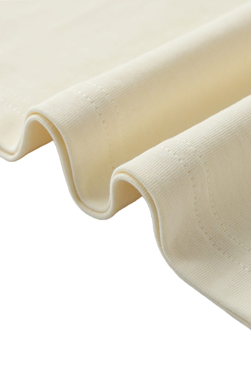 A close-up of the Crane Oversized Contrast-Stitched Cotton Tee in light beige, highlighting its visible edge stitching against a white background—an example of affordable luxury clothing.